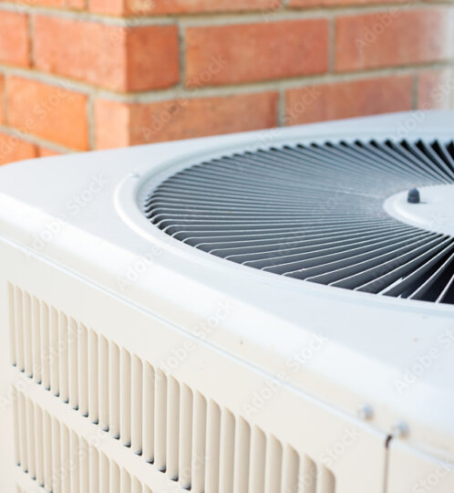 White outdoor air conditioner condenser with a circular top fan grille, mounted against a red brick wall.