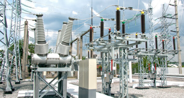 Outdoor electrical substation with large transformers, tall insulator stacks, metal frames, and overhead power lines under a cloudy sky.