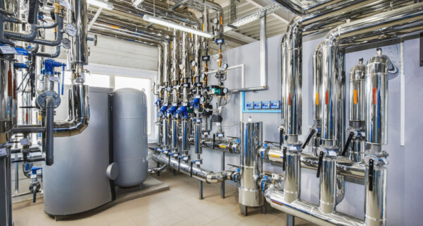 Industrial mechanical room with a complex network of polished stainless steel pipes, gauges, and large tanks.