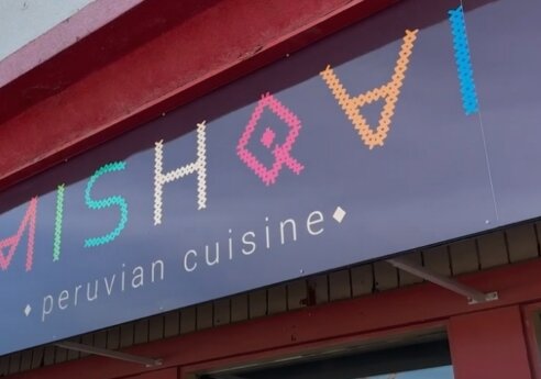 Storefront sign with colorful, dotted letters spelling the restaurant name and the subtitle "peruvian cuisine" beneath on a blue panel.