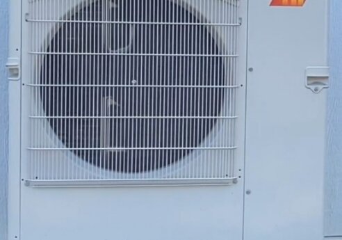 Outdoor Mitsubishi Electric air conditioner condenser with a large circular fan behind a protective grille, mounted on a metal frame.