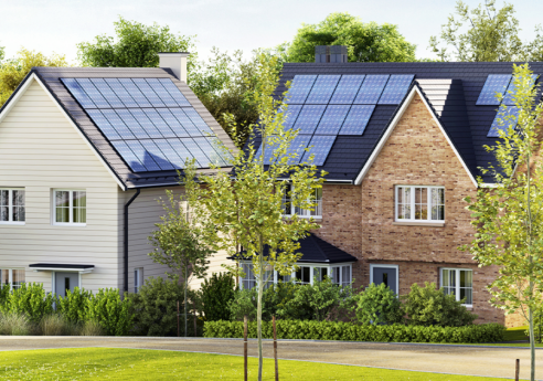 Two modern houses in a suburban setting with solar panels on their roofs, surrounded by trees, shrubs, and a neatly kept lawn.