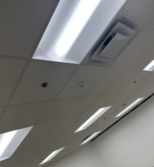 Empty room with a drop ceiling of fluorescent panels, white walls, and a small object on the bare concrete floor.