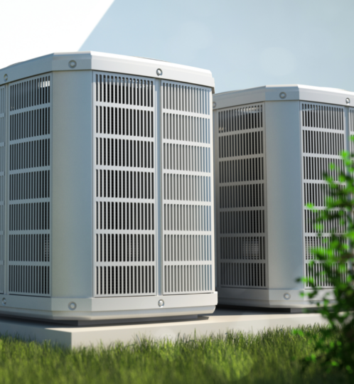 Two gray outdoor air conditioning condensers with vented panels sit on a grassy roof under a blue sky.