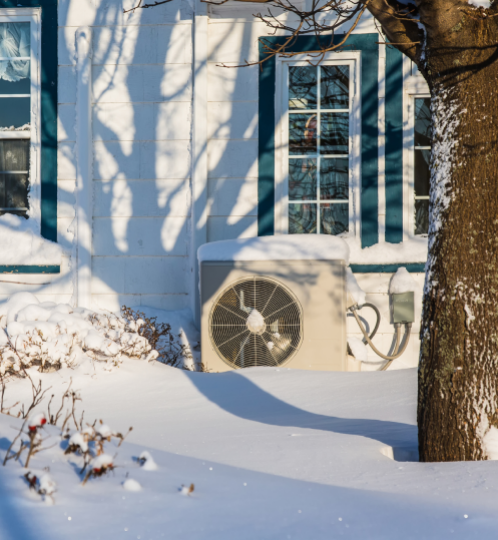 Snow covers the ground outside a light-blue house with teal-trimmed windows; a large outdoor HVAC unit sits against the wall, while tree shadows cross the facade.