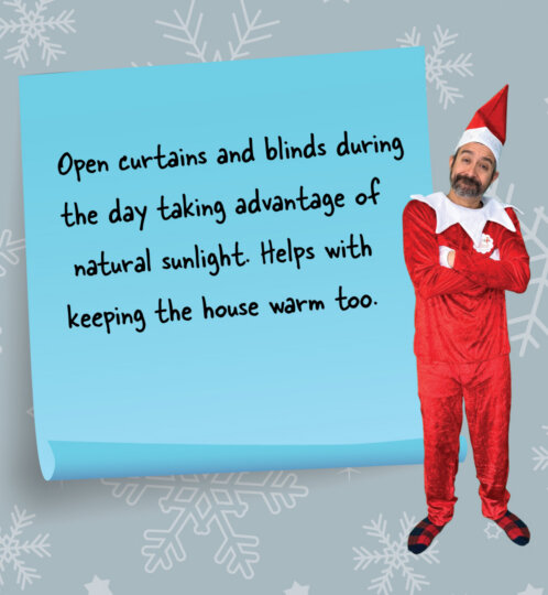 Blue sticky note with handwritten message about opening curtains for daylight and warmth, beside a person in a red elf costume against a snowy background.