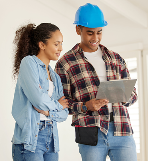 Two people indoors, one wearing a blue hard hat and plaid shirt, the other in a denim shirt, looking at and discussing a tablet together.