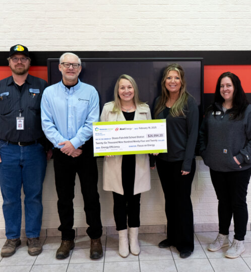 Five people stand in a hallway in front of a red-and-black Thunder banner, holding a large ceremonial check.