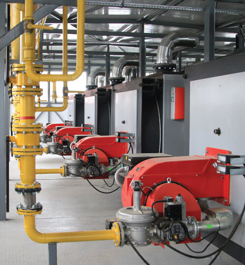 Industrial utility room with yellow pipes, red machinery, gray panels, and overhead silver ductwork.