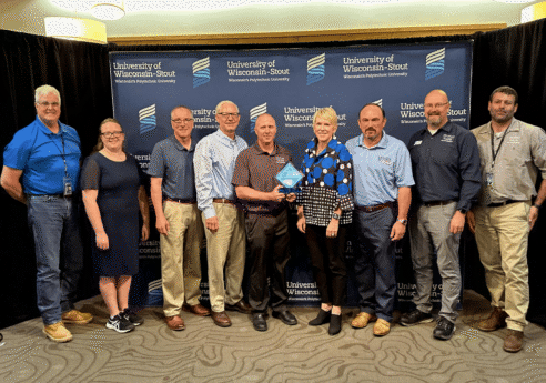 Group of people posing with a blue glass award in front of a University of Wisconsin-Stout backdrop, all dressed in business casual.