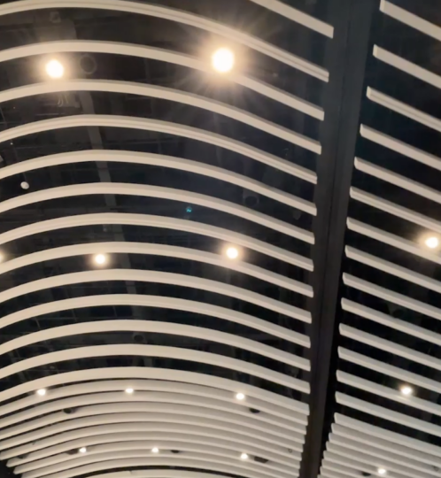 Interior ceiling with curved white slats forming a wave pattern against a dark background, with small recessed lights.