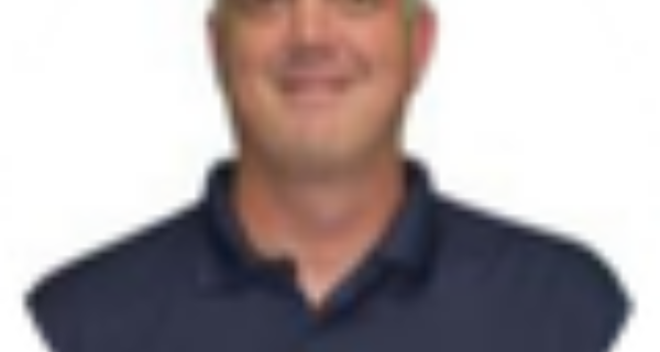 Smiling person with short light hair wearing a dark blue polo, shown in a circular portrait against a white background.