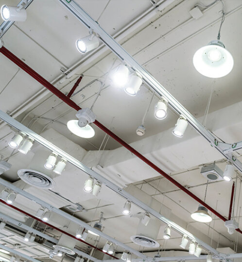 Industrial ceiling with numerous track lights and round hanging fixtures, red support pipes, and exposed ductwork.