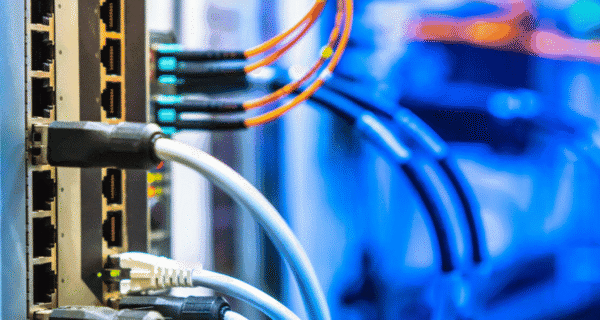 Close-up of a network switch with multiple Ethernet ports and plugged-in cables, set against a blue blurred data-center background.
