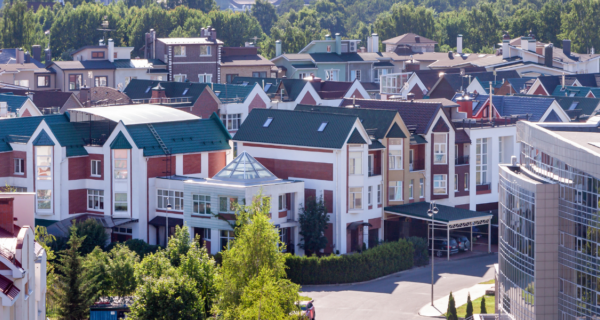 Row of colorful townhouses with steep gabled roofs, a curved glass office building to the right, and green trees in a suburban neighborhood.