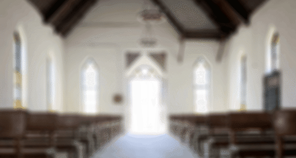 Blurred interior of a church with wooden pews on both sides and tall arched windows, bright light at the doorway at the far end.