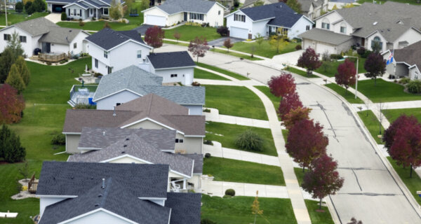 Aerial view of a suburban neighborhood with a curved street, row of two-story houses, green lawns, and trees with red and orange leaves.