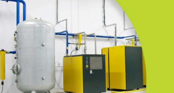 Industrial equipment in a clean facility: a large gray vertical tank, blue piping, and two yellow machines, with a lime-green curved overlay and a logo in the bottom right.