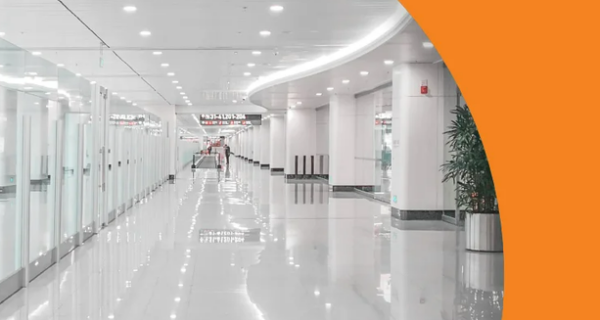 Orange brochure cover featuring a circular photo of a bright white office hallway with ceiling lights; 2024 BUSINESS OFFERINGS and LIGHTING, Focus on Energy logo.